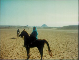 Scanned photo of Mary Mimi Hassouna riding in Egypt by the pyramids. 